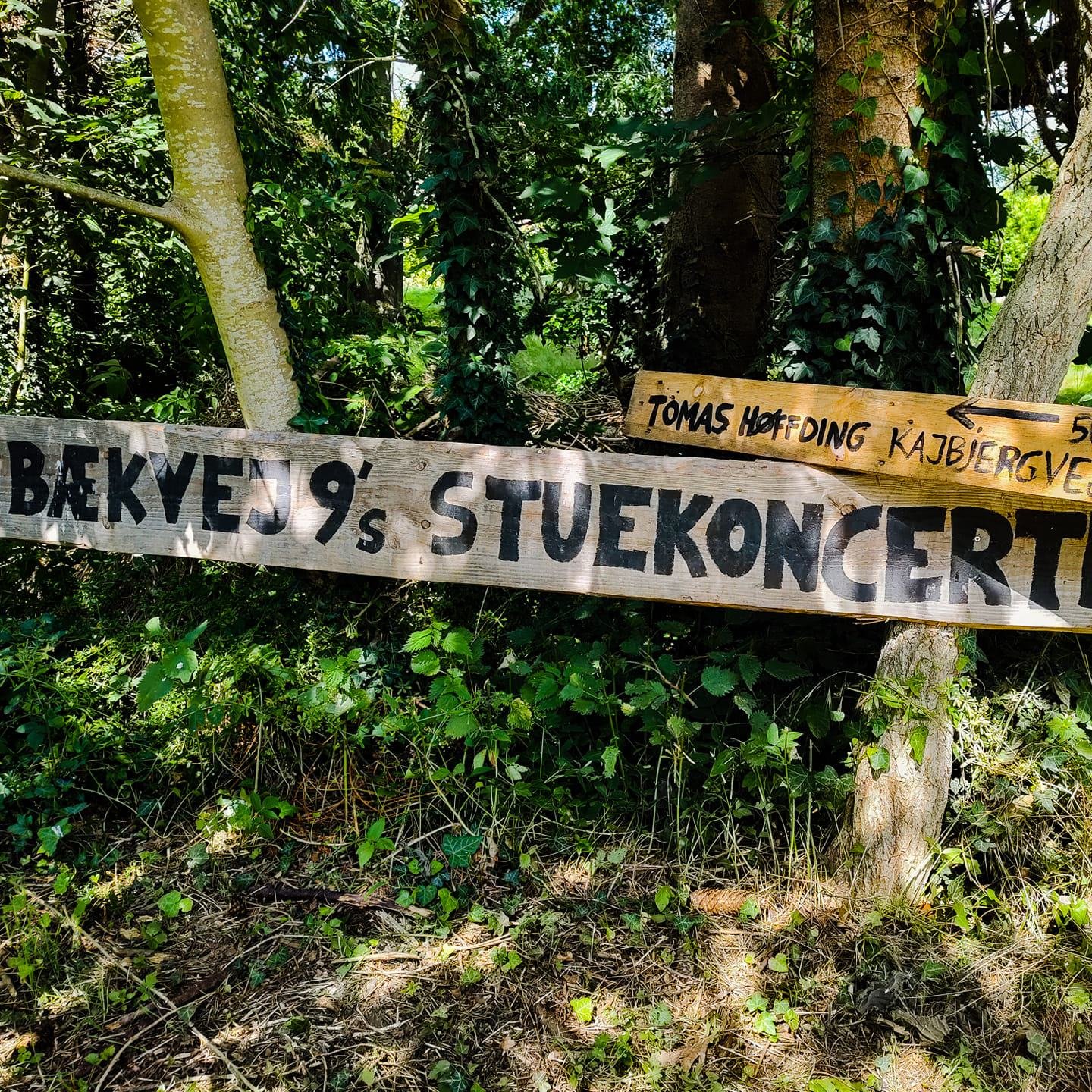 Skilt lavet af træ. Påmalet står "Bækvej 9's Stuekoncerter".