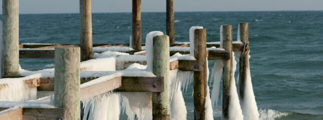 Foto af badebroen ved Tårup Strand om vinteren. Dækket er pillet af, men der er is og istapper på strøerne og stolperne.